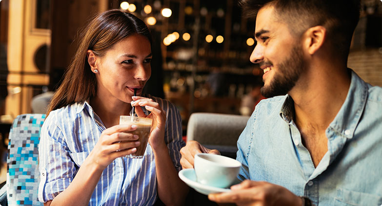 woman sipping drink smiling at man in cafe